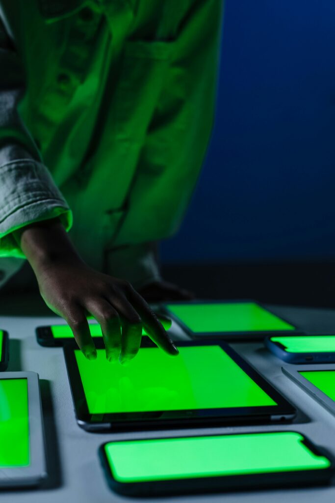 A hand interacts with multiple green screen electronic devices in a dimly lit room.
