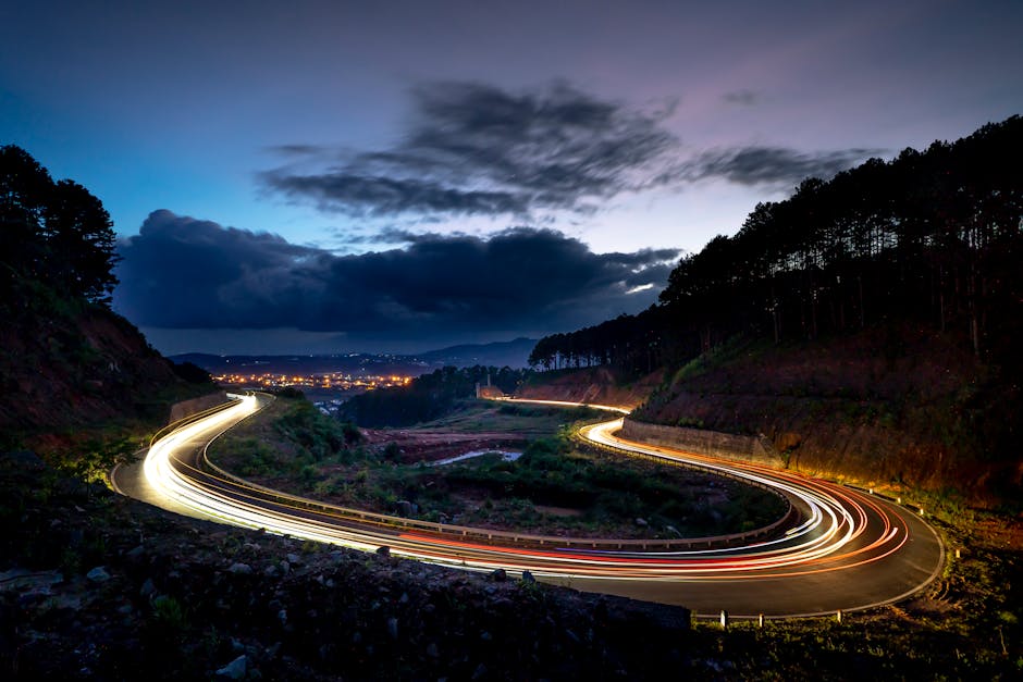 Captivating long exposure of a winding road at twilight with vivid light trails and a scenic landscape.