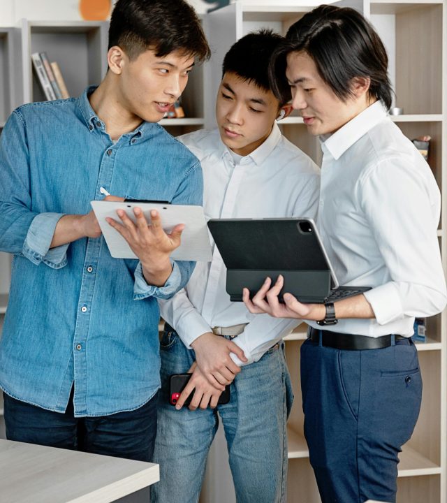 Three Asian men collaborate using digital tablets in a modern office space.